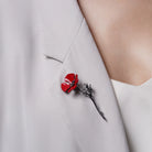 Red enamel poppy brooch with a dark metallic stem worn diagonally on a light blazer lapel.