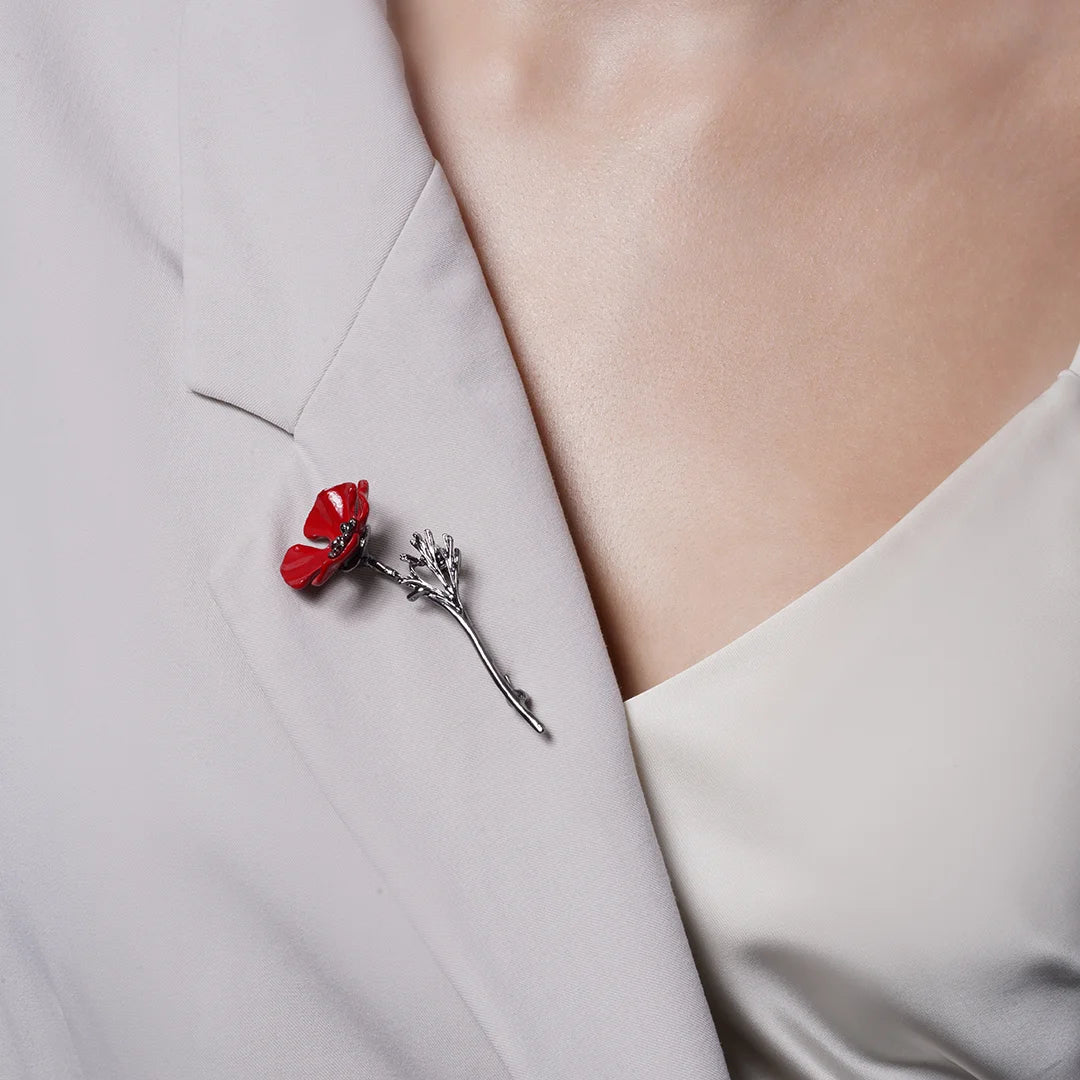 Red enamel poppy brooch on a light blazer lapel, wider view showing its size when worn.